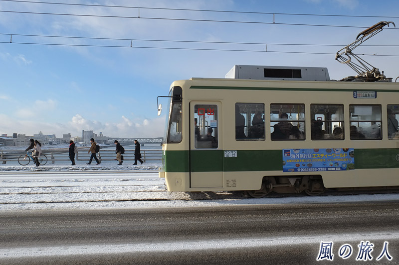 歩く人々と路面電車　凍結の新己斐橋の写真